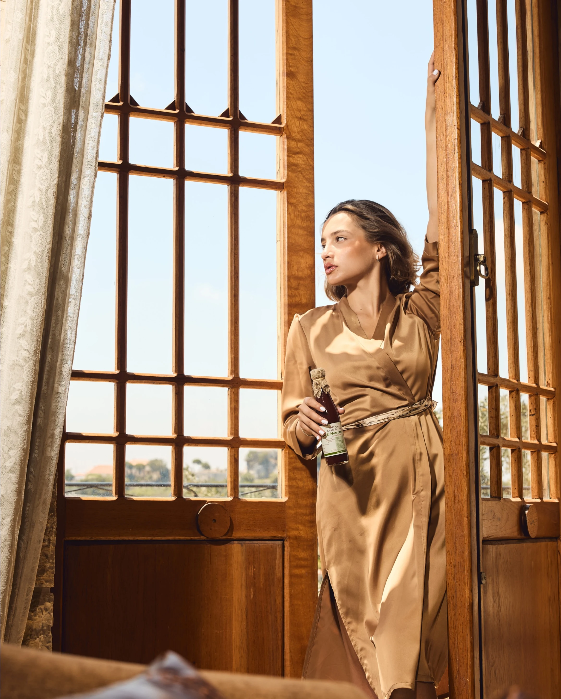 Woman holding a Magharet Jeita bottle in a sunlit wooden doorway